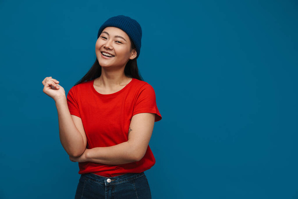 Happy young asian woman in casual clothes standing over blue wall background, looking at camera - Valokuva, kuva