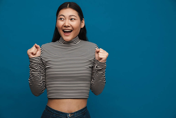 Excited asian teen girl gesturing and laughing at camera isolated over blue background - Zdjęcie, obraz