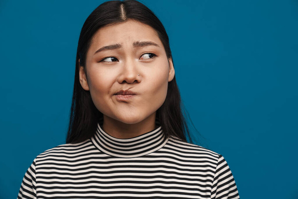 Displeased asian teen girl posing and looking aside isolated over blue background - Foto, Imagem