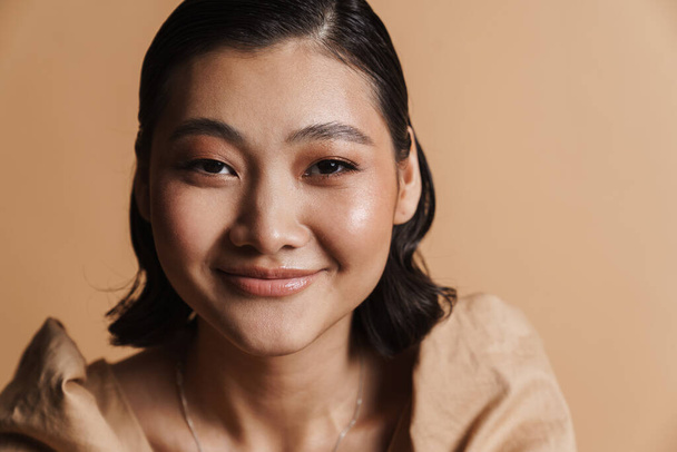 Young asian brunette woman smiling and looking at camera isolated over beige background - Fotografie, Obrázek