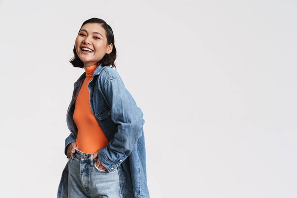 Happy smiling young asian brunette woman in denim jacket posing standing over gray background - Φωτογραφία, εικόνα