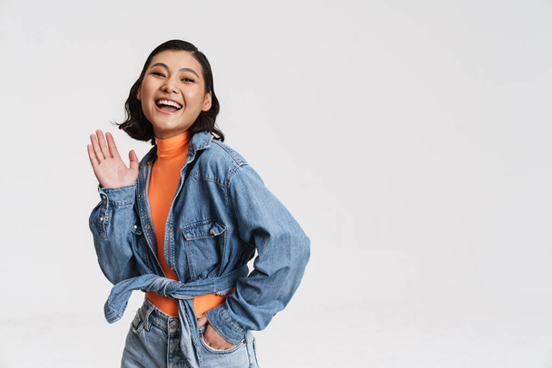 Happy smiling young asian brunette woman in denim jacket posing standing over gray background - Zdjęcie, obraz