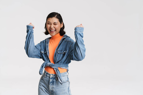 Young asian brunette woman screaming while making winner gesture isolated over white background - Photo, Image