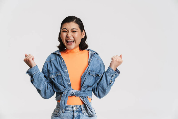 Young asian brunette woman screaming while making winner gesture isolated over white background - Foto, Imagem