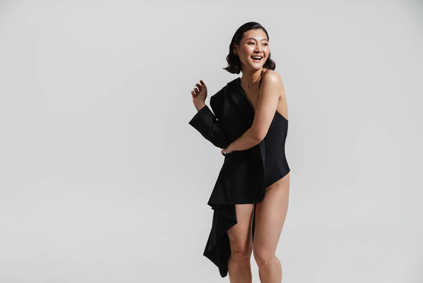 Brunette asian woman wearing swimsuit and jacket smiling at camera isolated over white background - Photo, Image