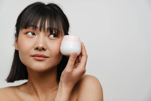 Young asian shirtless woman posing with face cream isolated over white background - Photo, Image