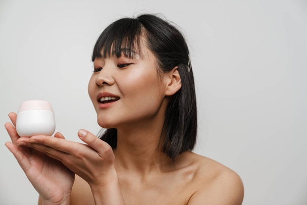 Young asian shirtless woman posing with face cream isolated over white background - Foto, immagini