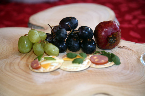Christmas. Appetizers on a cutting board for a Christmas. Appetizers consisting of cheeses, fruits, sausages, crackers and fresh herbs. Wooden Tree Stump Cutting board. Christmas Snacks. Meat and Cheese and Fruit Snacks. Wooden cutting board. Snacks. - Photo, Image