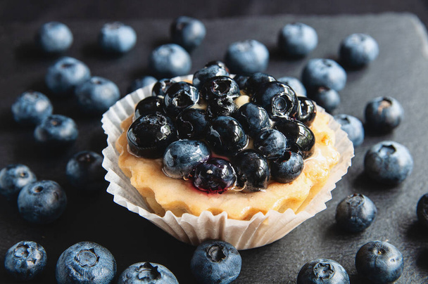 Tart with blueberries is on a black background of natural stone. Still life with sweet cakes with wild berries on a dark background - Zdjęcie, obraz