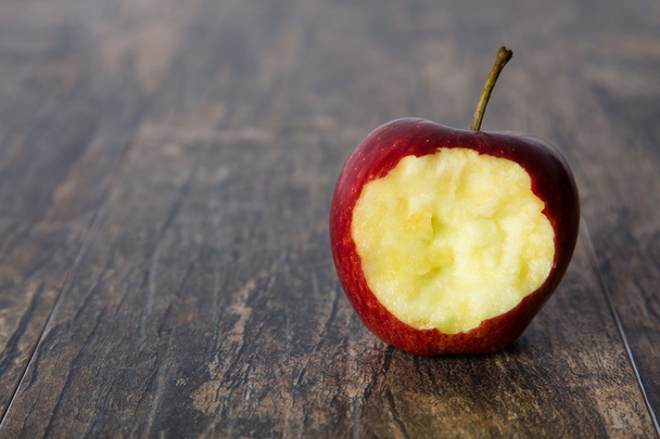 Red apple with a hole bitten into it on a brown surface - 写真・画像