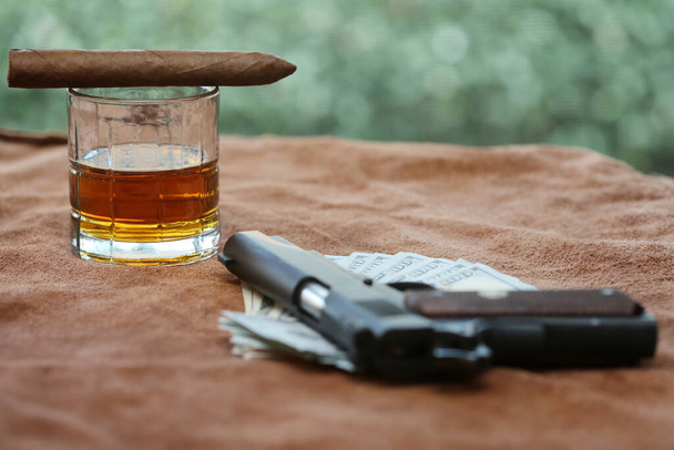 Cigar. Cuban Cigar, Whiskey, Cash, Poker Hand, and a Hand Gun on a Leather background. Poker player with gun, showdown with opponents. Poker player with gun plays in casino. Dead mans hand aces and eights with Pistol, Whiskey and a Cigar.   - Photo, Image