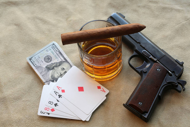 Sikari. Kuuban sikari, viski, käteinen, pokerikäsi ja käsiase nahkataustalla. Pokerinpelaaja aseen kanssa, välienselvittely vastustajien kanssa. Pokerinpelaaja, jolla on ase pelaa kasinolla. Kuolleet miehet käsi ässät ja kasit kanssa Pistooli, Viski ja sikari.   - Valokuva, kuva