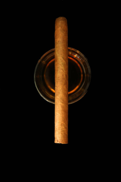 Whiskey and Cigar. Fine Whiskey and Cuban Cigar on black velvet. Room for text over lay. Snifter glass of cognac and cigar. Glass of whiskey and smoking cigar on table. Copy space, black background. Whiskey, brandy, cognac, alcoholic drink . Luxury.  - Photo, Image
