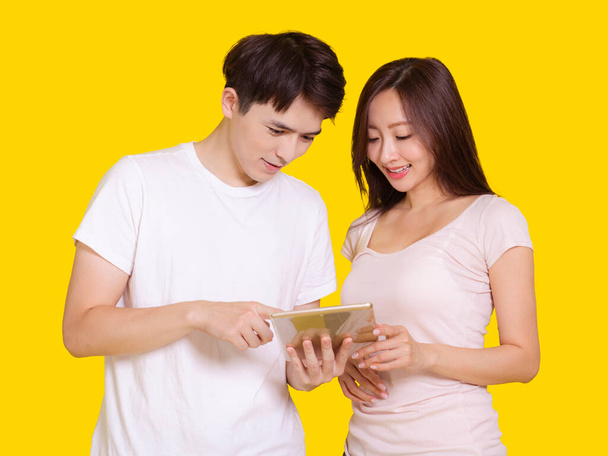 Молодий чоловік і жінка використовують планшетний комп'ютер. Ізольовані на жовтому тлі
. - Фото, зображення