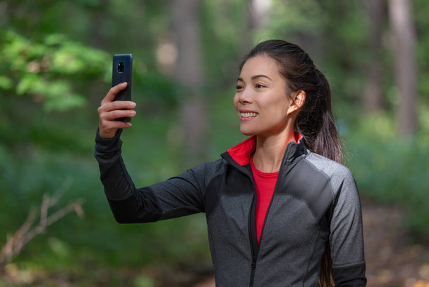 Phone active woman taking picture with mobile cellphone outside on forest nature walk during cardio activity holding smartphone - Foto, afbeelding