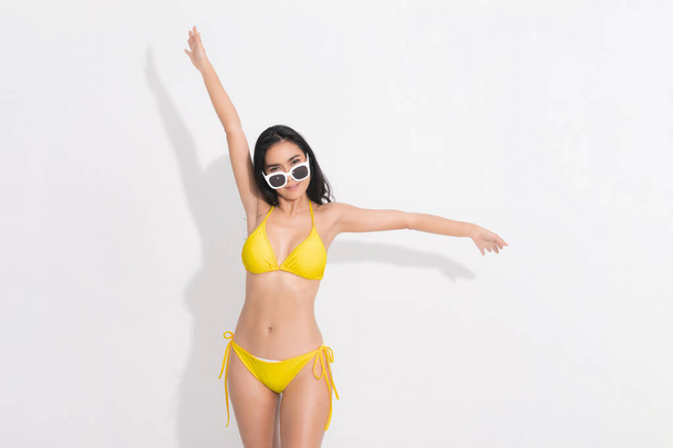 Mulher vestindo um vestido de biquíni amarelo e óculos de sol brancos na cabeça em conceito moda verão, espalhar seus braços expressando estúdio felicidade filmado em fundo branco isolado. - Foto, Imagem