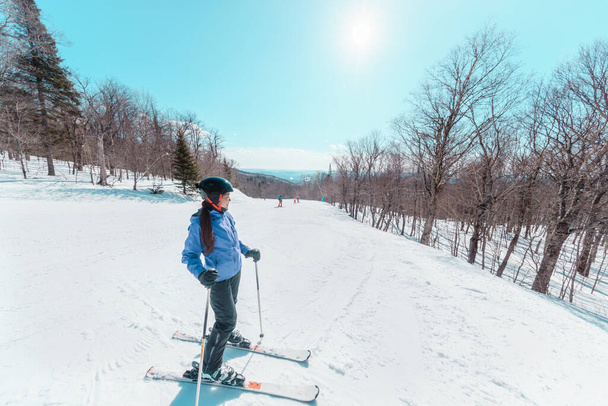 Skier woman taking a break during skiing on slope. Happy Asian active woman relaxing on sunny day at ski resort. Winter sport holiday - Photo, image