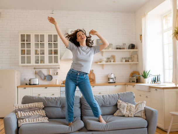 Young woman jumping on the sofa at home. - Φωτογραφία, εικόνα
