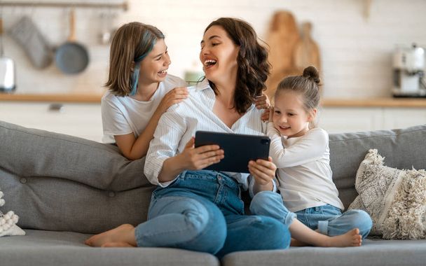 Happy loving family. Young mother and daughters girls using tablet pc for remote conversation with friends. Funny mom and lovely children are having fun staying at home. - Photo, Image