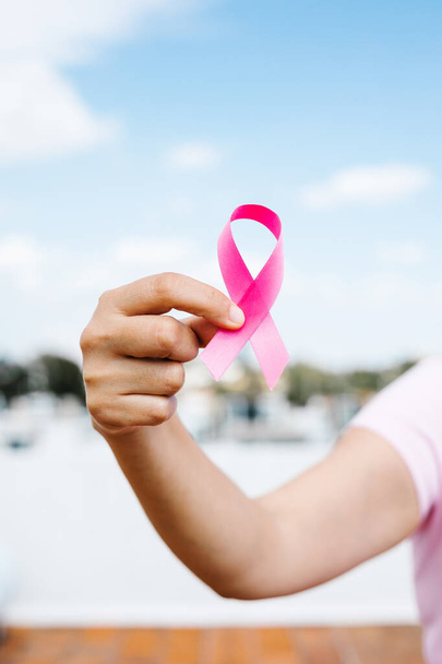女性の手を保持ピンク乳癌意識リボンで青い空で背景としてラテンアメリカ - 写真・画像