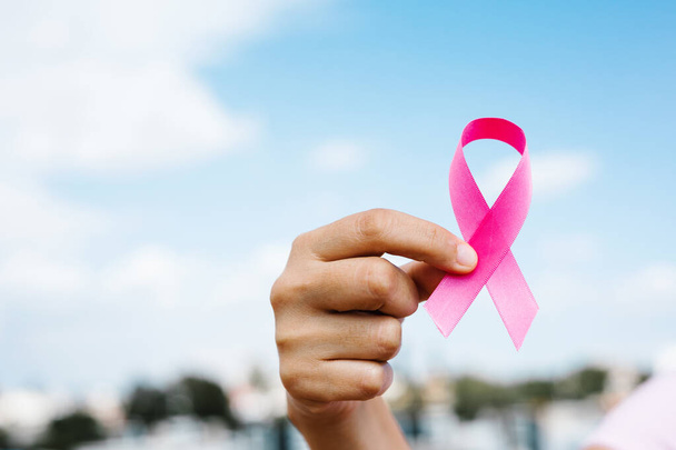 kobieta ręce trzymając różowe wstążki świadomości raka piersi z niebieskim niebem jako tło w Ameryce Łacińskiej - Zdjęcie, obraz