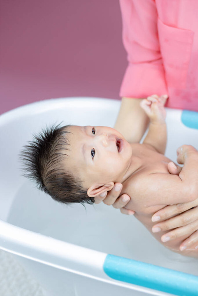 Recém-nascido tendo um banho na bacia pela mãe rosa fundo - Foto, Imagem