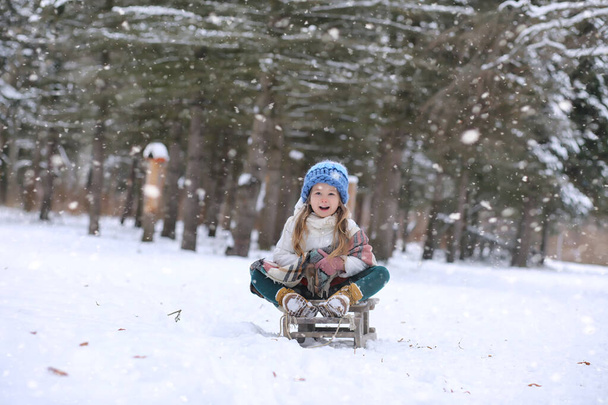 Winter sprookje, een jonge moeder en haar dochter rijden een slee in het bos. Een meisje op een slee met geschenken aan de vooravond van het nieuwe jaar in het park. Twee zussen lopen in een nieuwjaarspark en rijden op een slee met geschenken - Foto, afbeelding
