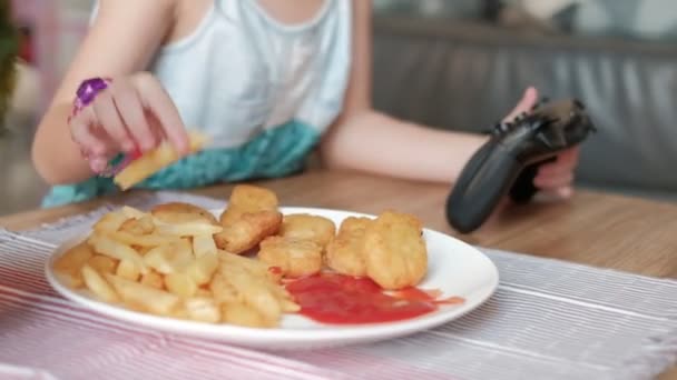 Nahaufnahmen von VDO zeigen, wie Kinder Fast Food essen und Joystick zum Spielen von Videospielen zwingen, weißes Gericht mit Pommes, Nuggets und Ketchup. Online-Unterhaltungstechnik macht Kinder süchtig. - Filmmaterial, Video
