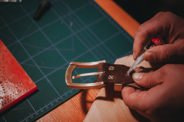 A closeup shot of hands sticking the metal parts of the brown leather belt with the glue - Foto, Imagem