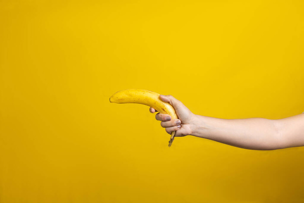 A female hand holding ripe banana isolated on a yellow background - Foto, afbeelding