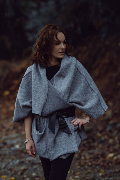 A curly short-haired Caucasian woman wearing a grey coat in the autumn forest - Foto, immagini