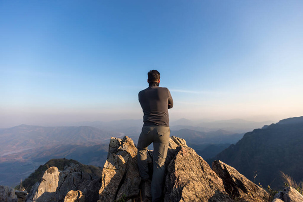 Young Man Standing on the edge of a cliff and enjoys the sunrise. Backpacker in a hike in the summer mountains. A young man on top of the mountain - Φωτογραφία, εικόνα