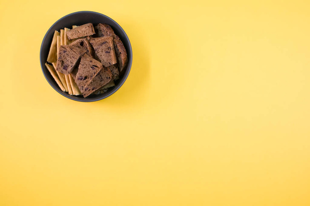 A top view of the tasty salty crackers with slices of brown bread in the bowl on the yellow surface - Fotoğraf, Görsel
