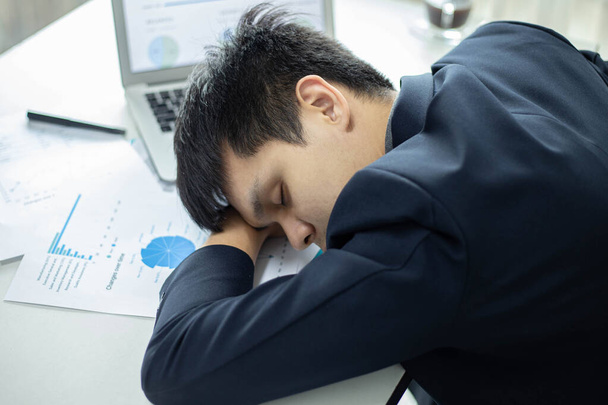 Zakelijke partners concept een mannelijke jonge zakenman slapen op een bureau met een laptop en document na lange tijd te hebben gewerkt. - Foto, afbeelding