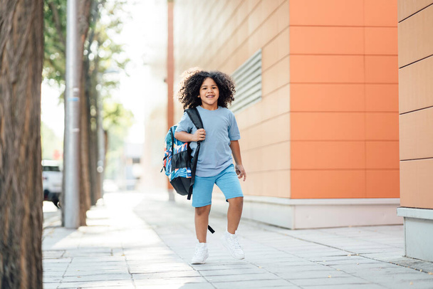 niño pequeño, pelo afro caminando con mochila de vuelta a la escuela feliz de ir a clase - Foto, Imagen