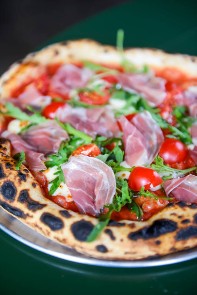 Pizza prosciutto with ham, tomato and mushrooms served on a round tray on a table inside a restaurant. Traditional Italian pizza recipe. - Fotó, kép