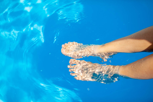 Yaz tatili kavramı. Havuzun mavi suyunun arka planında genç bir kadının bacakları. Havuzda yüzmek. Rahatlama, güneş banyosu ve neşe. - Fotoğraf, Görsel