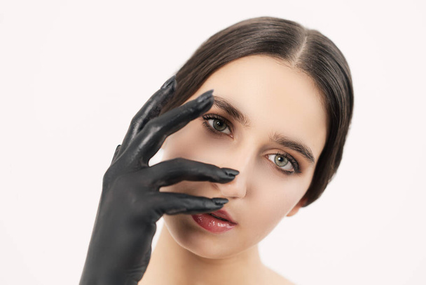 Light-skinned girl with a black hand from the paint. Looking straight into the camera is covered by the hand. - Fotografie, Obrázek