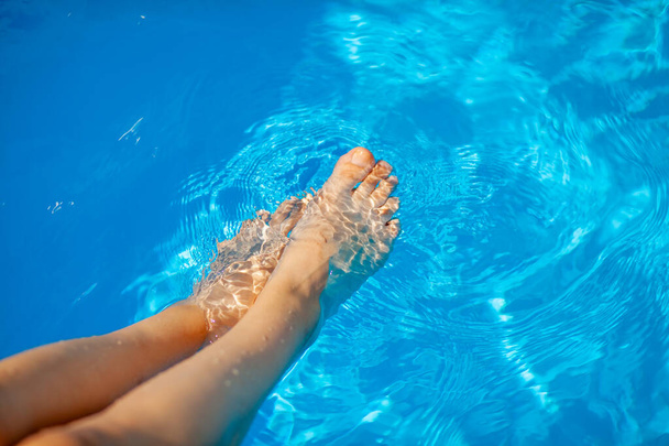 Yaz tatili kavramı. Havuzun mavi suyunun arka planında genç bir kadının bacakları. Havuzda yüzmek. Rahatlama, güneş banyosu ve neşe. - Fotoğraf, Görsel