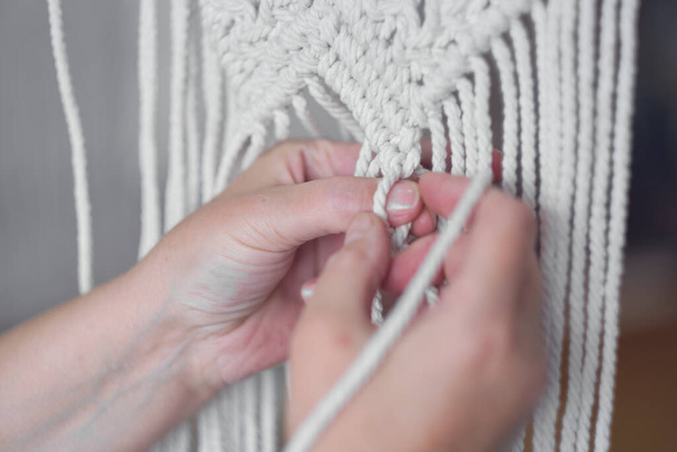 base knots of macrame, the view from behind the shoulder close-up of the women hands, she ties knots. ECO friendly modern knitting DIY natural decoration concept. - Фото, изображение