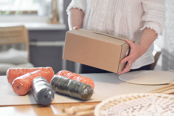 woman entrepreneur packs a handmade product in a cardboard box. delivery of goods for a small business. an elderly woman earns her hobby from home. - Zdjęcie, obraz