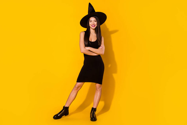 Full body photo of nice witch millennial lady crossed arms stand wear black dress cap shoes isolated on yellow color background - Фото, изображение