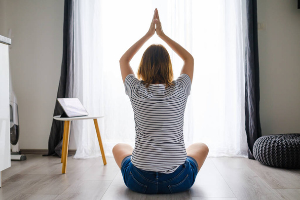 Mujer joven medita o practica yoga en la sala de estar utilizando la aplicación de entrenamiento en línea la tableta  - Foto, imagen