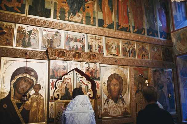 Ortodoksinen kristitty pappi ja seurakuntalainen rukoilemassa kirkon ikoneja. - Valokuva, kuva