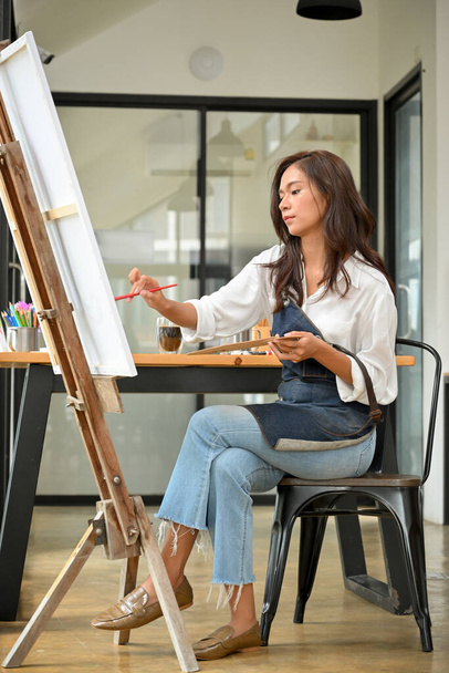 Inspired artist woman using paintbrush drawing on canvas easel, creative occupation, female painter - Photo, Image