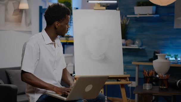アートスタジオでラップトップコンピュータを保持している黒の創造的なアーティスト - 写真・画像