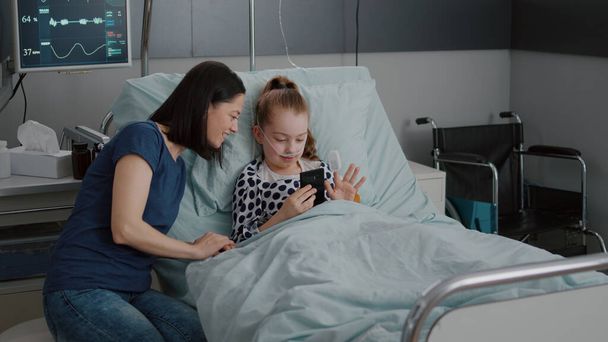 Moeder en zieke dochter groeten vrienden met online videocall telecommunicatie - Foto, afbeelding