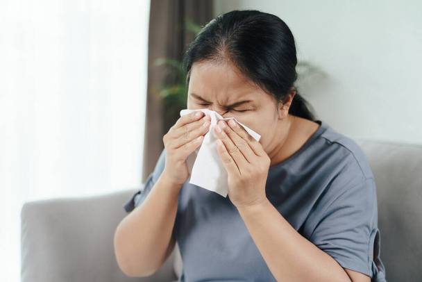 La mujer enferma de frío tiene tos alérgica en la nariz o estornuda con papel tisú sentado en el sofá. Salud y concepto médico - Foto, Imagen