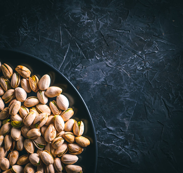Pistachios in a black plate on a dark table. Ready to eat nuts. Energy food.  - Foto, Imagen