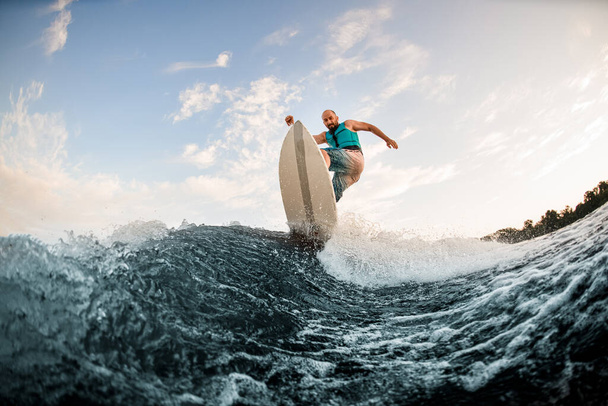 sportive man effectively jumps on wakeboard over splashing wave. Wakesurfing on the river. - Fotografie, Obrázek